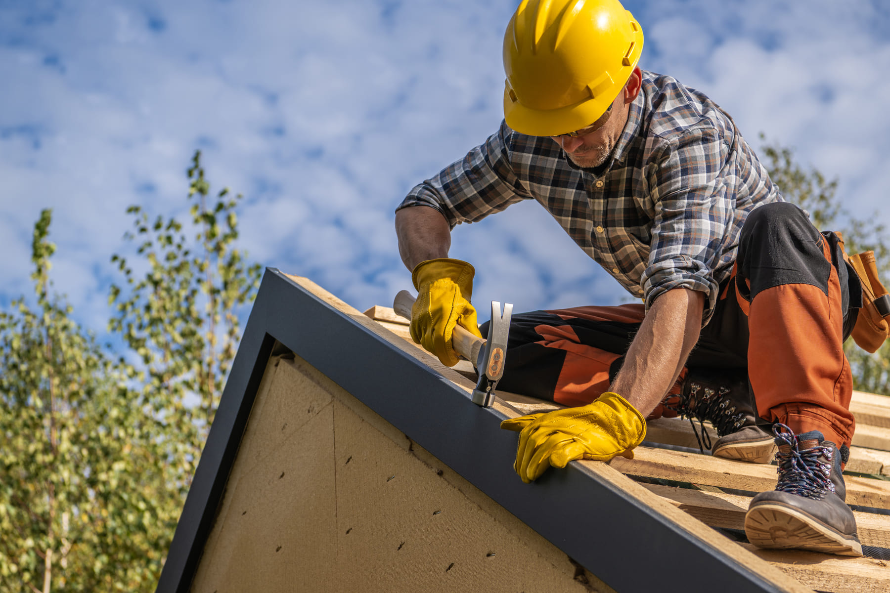 Roofer hammering shingles on a rooftop in bright sun